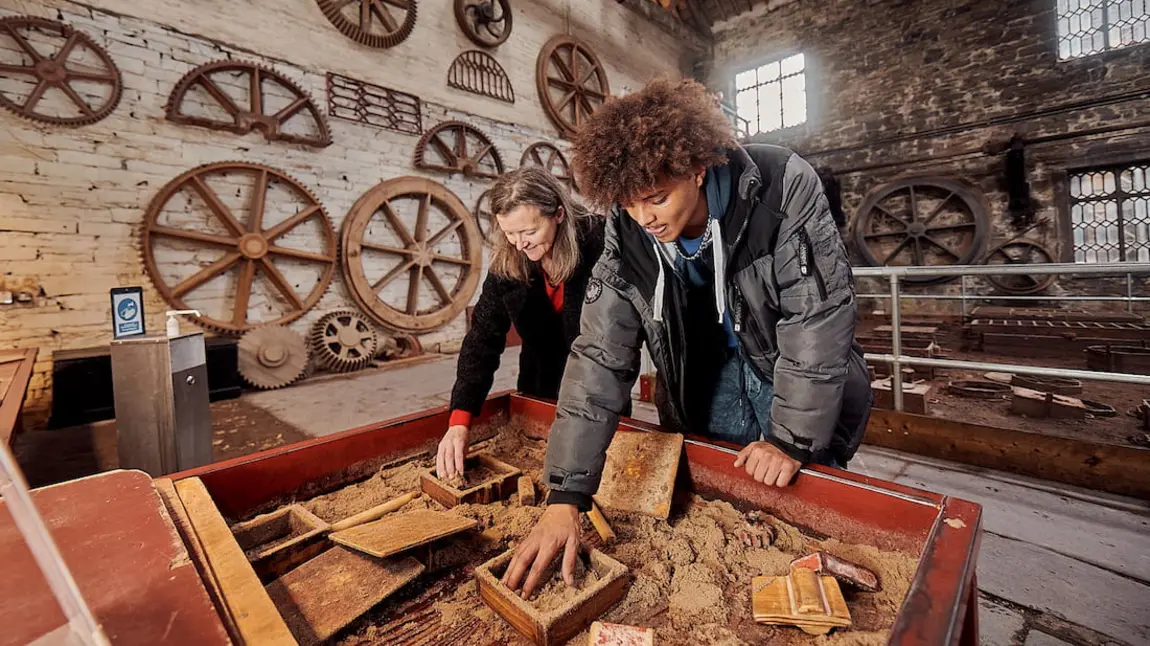 Two people do an activity in the foundry building, a large brick industrial building at the National Slate Museum in Wales