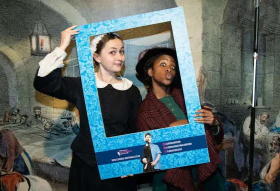 Two people in historic nursing outfits depicting Mary Seacole and Florence Nightingale, holding a frame to their faces
