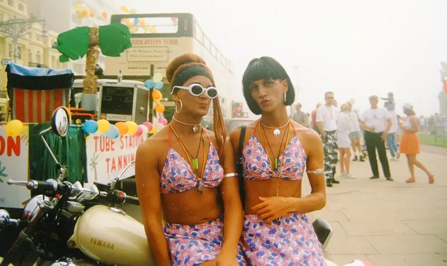 Two people wearing vibrantly patterned beachwear pose in front of a motorcycle