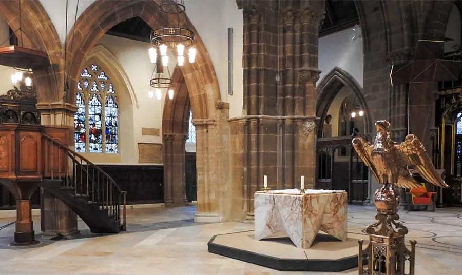 A photo taken inside Leicester Cathedral showing the altar, pulpit, lectern and the building's architecture including stone arches and columns