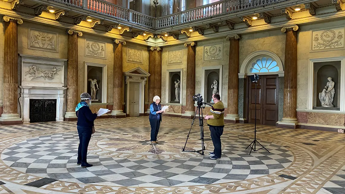 Three people recording film in large stately room