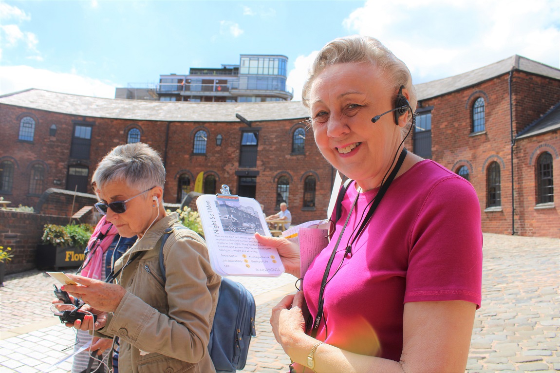 A tour guide holding a clipboard and radio, with the roundhouse in the background