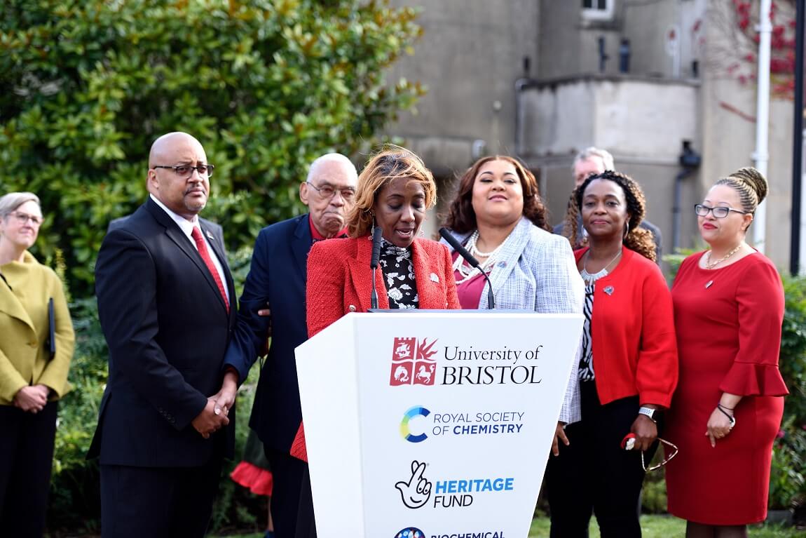 People gathered around a podium, behind someone giving a speech