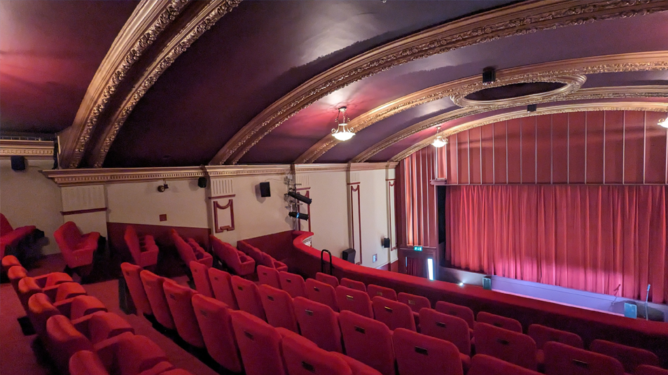 The inside of the cinema screen with rows of red seats, gold gilt arches across the ceiling and early 20th century light fittings