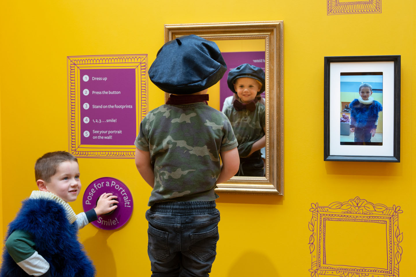 Two children dress up, one wearing a beret in front of a mirror