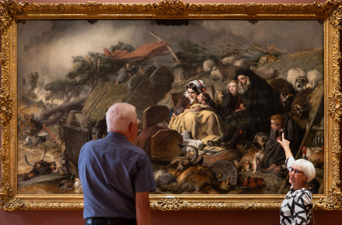 Two older visitors look at a huge painting of figures in an apocalyptic landscape