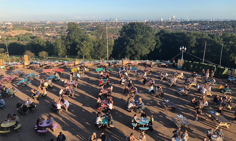 Large terrace full of people sitting around tables with fantastic view of London in background