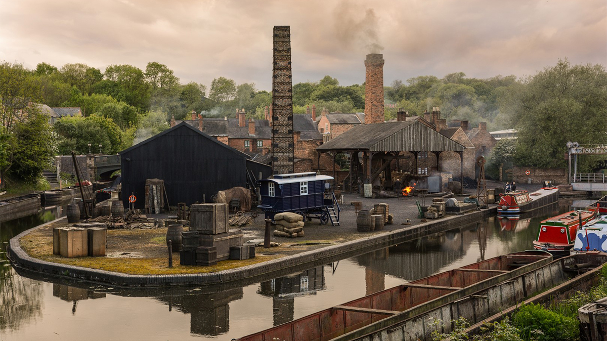 Buildings by side of canal. Chimeys smoking. Houses in background.