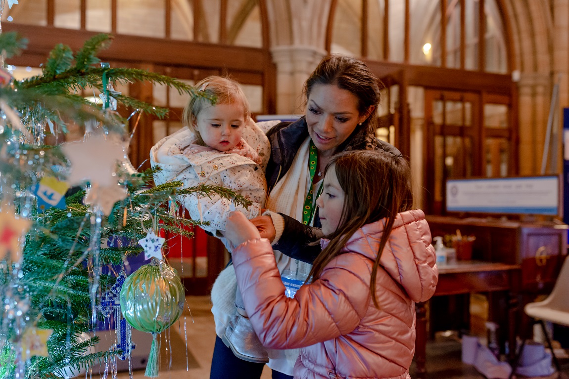 A young family hanging ornaments on a Christmas tree at Truro cathedral