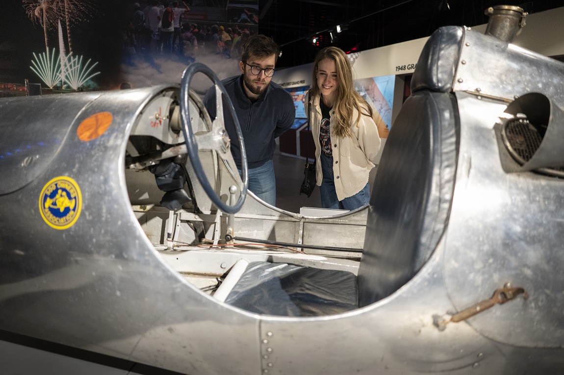 People looking at an exhibit of a motor car in a museum