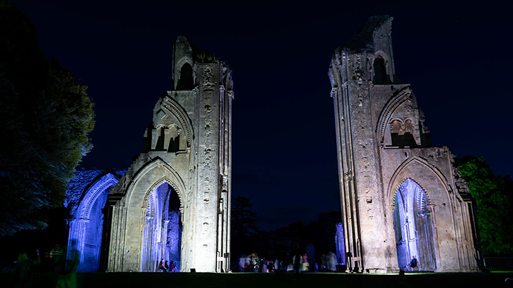 The two sections of Glastonbury Abbey nave at night lit with blue and violet lights