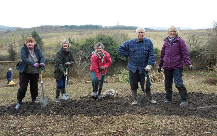 A group of people standing in a row in woodland with spades