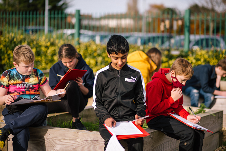 Children sitting in a garden, working on clipboards