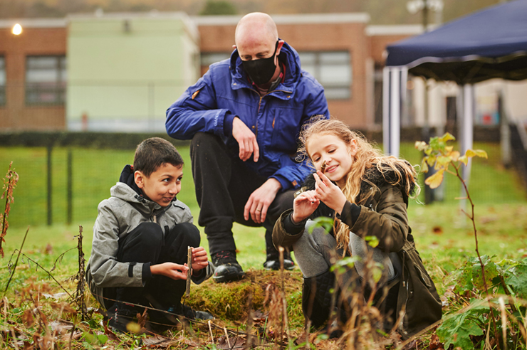 Two children looking at sticks while an adult watches