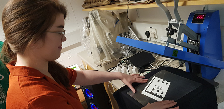 Young woman at a T-shirt printer with a design reading 'We should all be feminists'