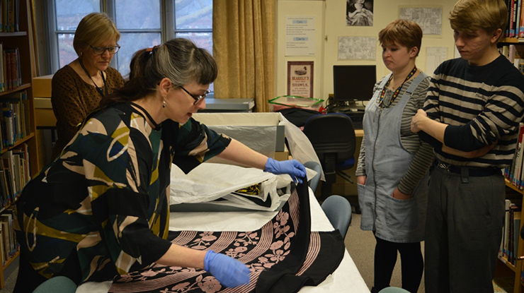 Three people watch a fourth wearing gloves who handles a piece of fabric.