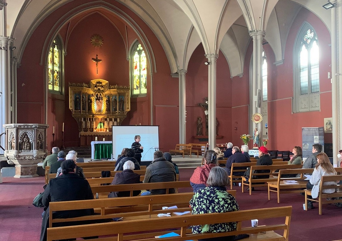 People attending a workshop in a church - guests sitting on pews while a speaker presents at the front