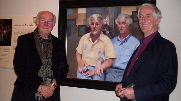 Two men standing next to a painting of themselves in an exhibition