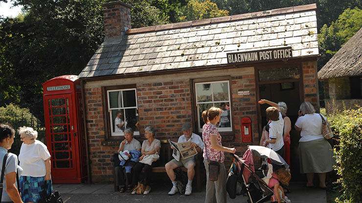 People mill outside a cottage post office and red telephone box