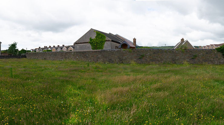 A stone house overlooks a meadow with flowers