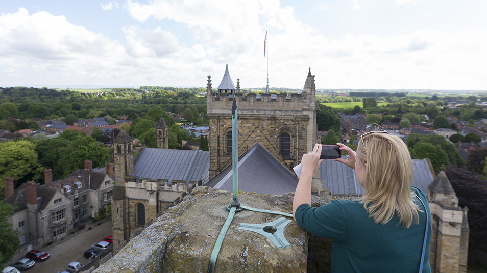 Woman standing on the roof of Ripon Cathedral, taking a photograph with a mobile phone