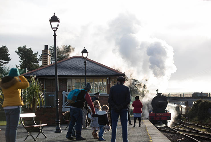 People stand on a railway platform as a steam train comes in