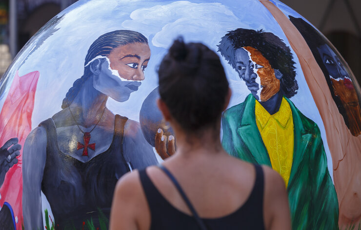 A person stands in front of The Echoes in the Present sculpture by Larry Amponsah