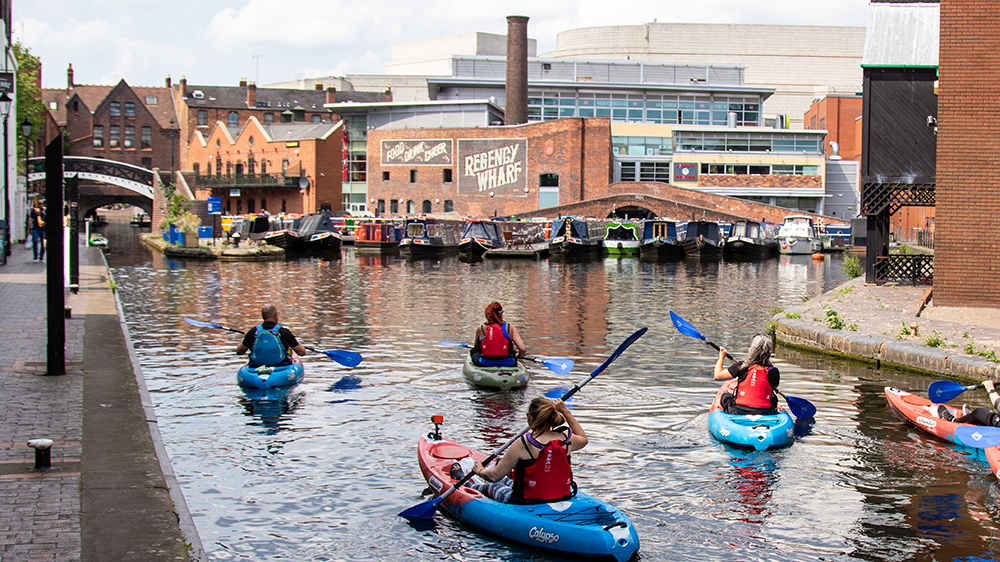 People kayaking on canal with historic buildings in background