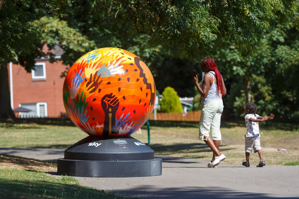 A woman and child look at a brightly coloured globe sculpture situated outdoors
