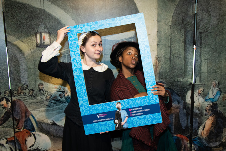 Two people dress up in period clothing and hold a frame in front of them whilst they pose for the camera.