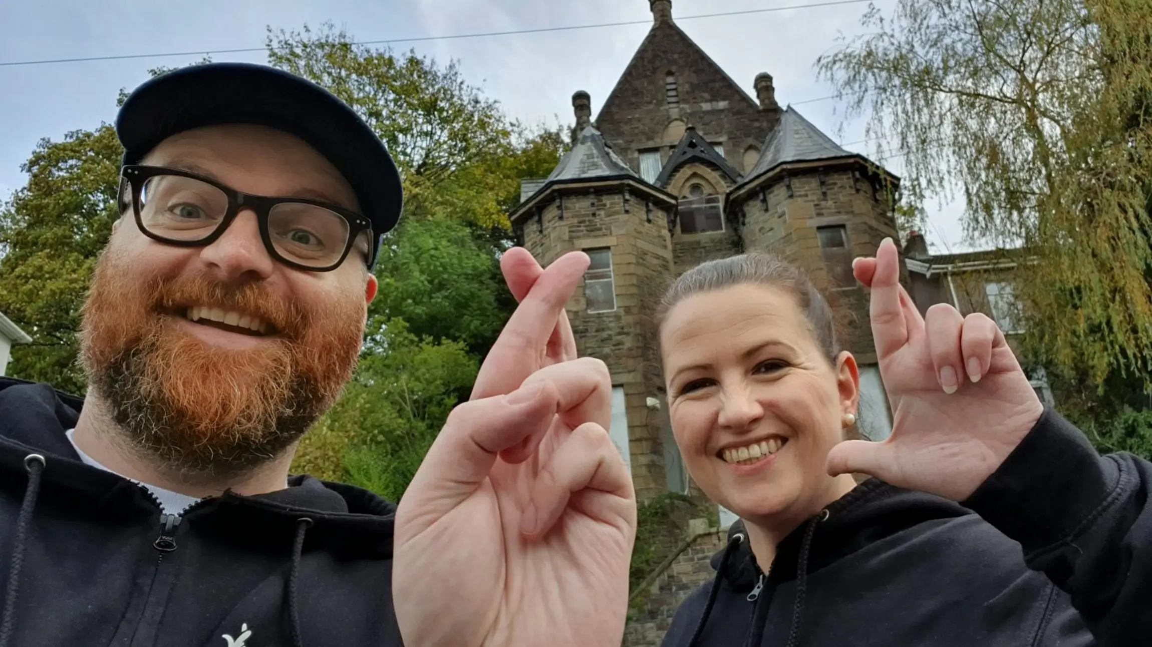 A Two people standingin front of a heritage site doing the crossed fingers selfie