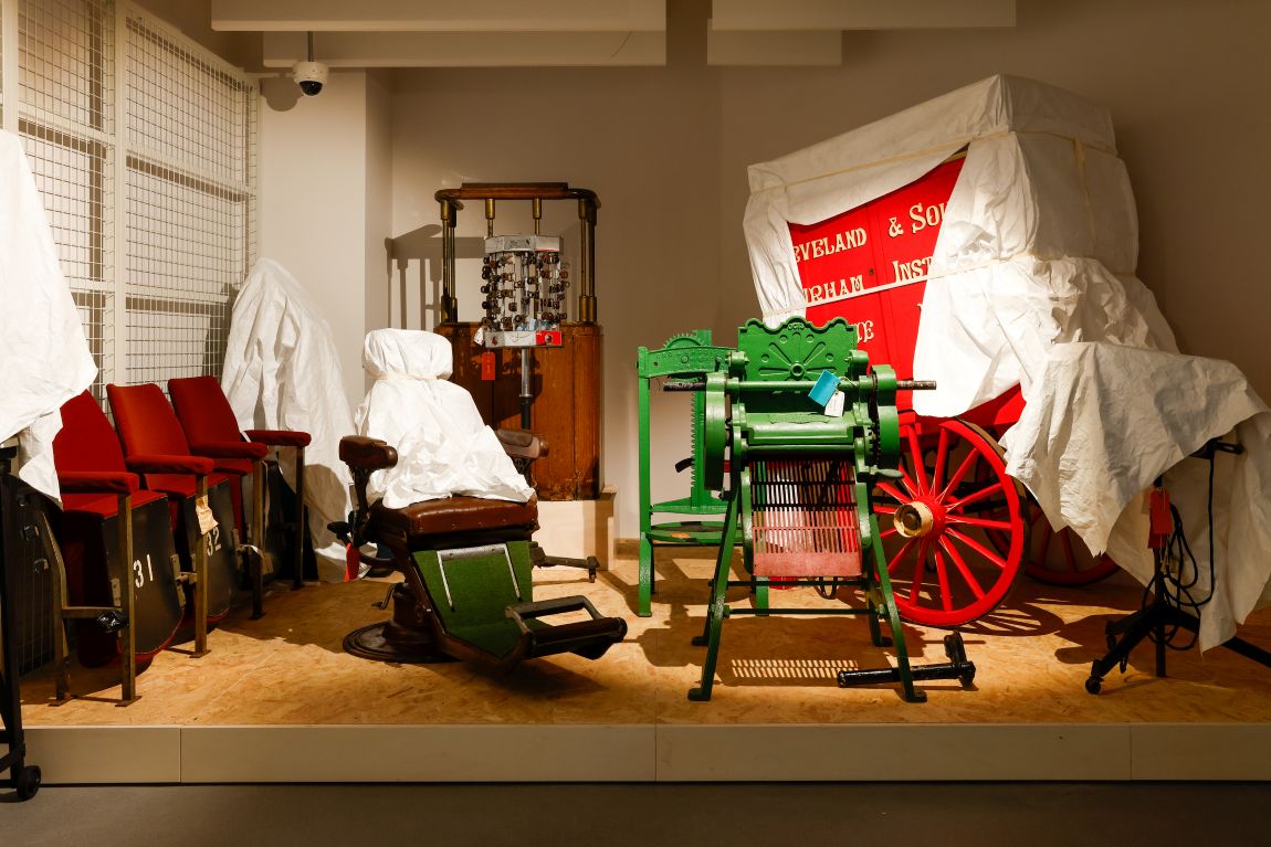 More objects, some under sheeting, in the Open Store, including a mangle, a barber's chair and a wooden wagon.