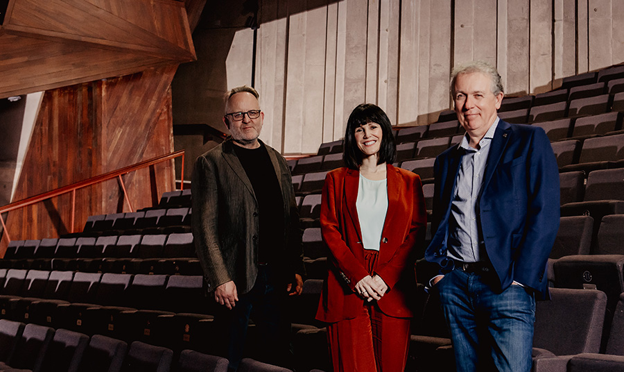 Three people are standing in a theatre with empty seats.