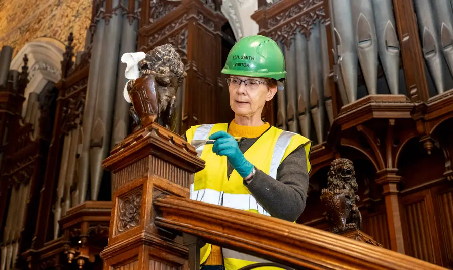 A volunteer using a paint brush to clean a wooden banister 