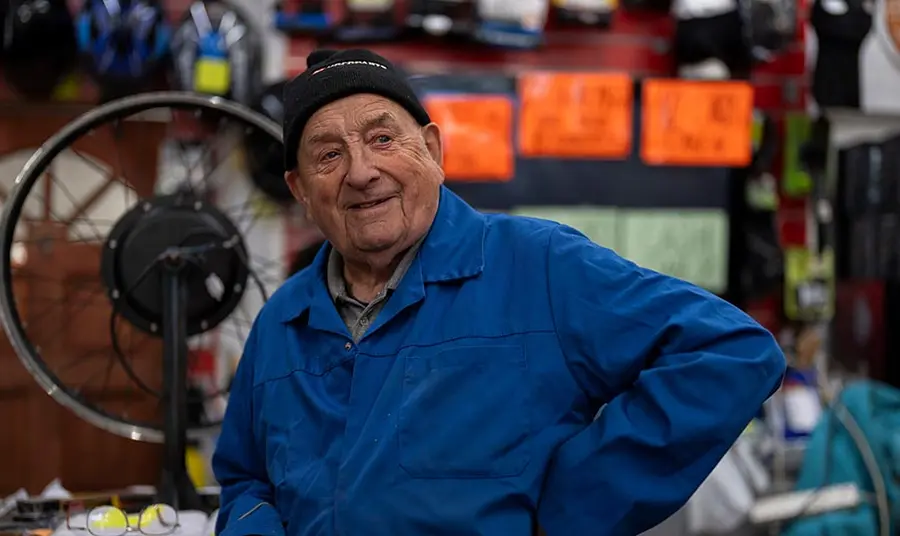 an older man wearing blue overalls in a bicycle repair shop