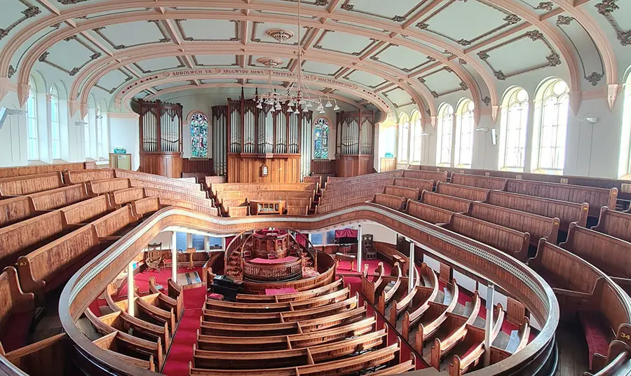 A large room containing a pipe organ and two levels of wooden seating