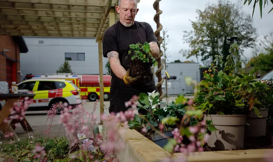 A man is doing some garden outside and fire vehicles can be seen in the background