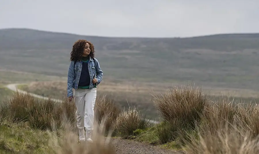 A young woman walks through a moorland landscape
