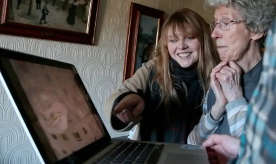 A yonuger person assisting an older person on a computer