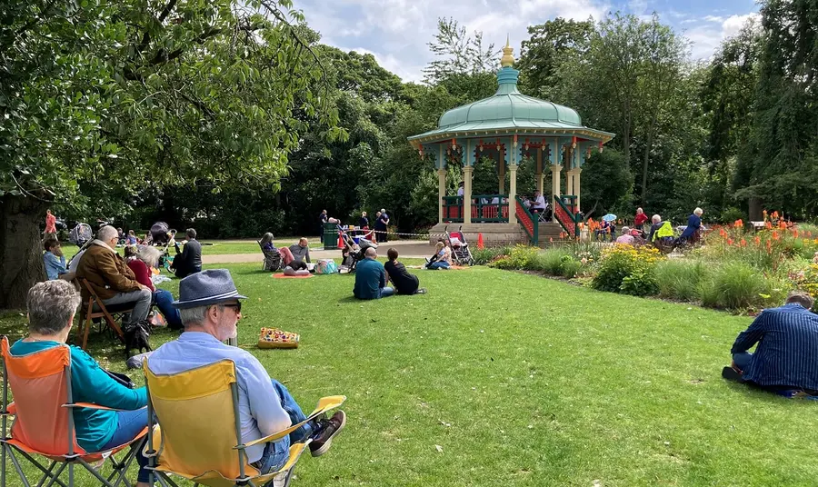 People sitting in a sunny park, near a bandstand