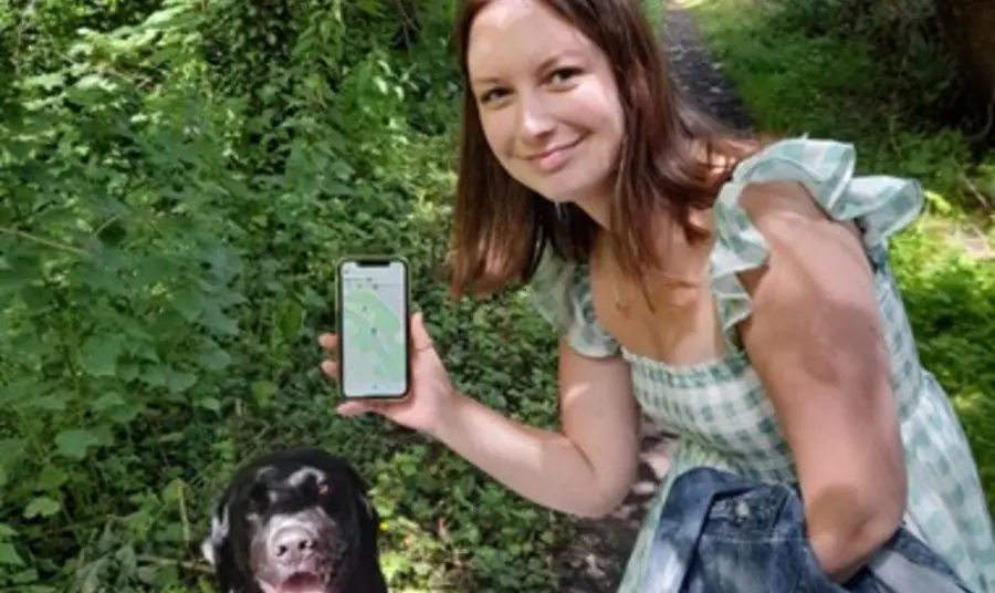 Hayley Melrose holding a phone showing a walking route with a dog in a woodland