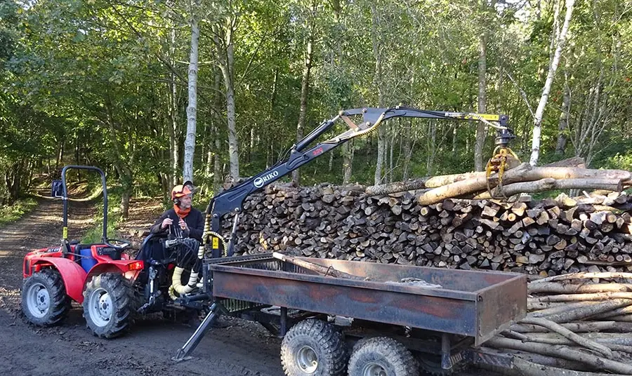 A person on red quad moving logs onto a trailer on a woodland path