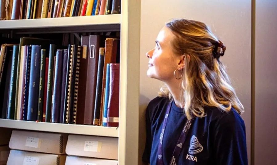 Kira Mills standing in an archive with packed bookshelves.