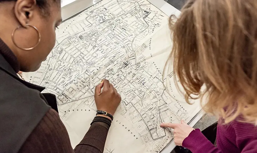 two people, one with dark skin and one with long blond hair, look at a map