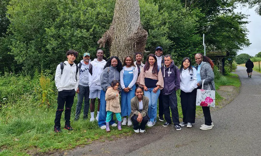 A group of people posing in front of greenery and a sculpture made of natural materials