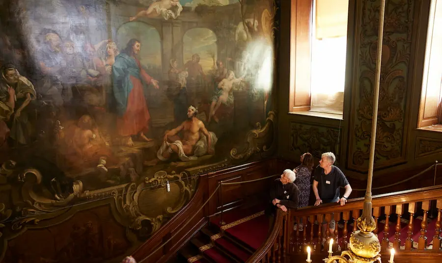 People are stood on stairs and looking up at a painting that covers an entire wall