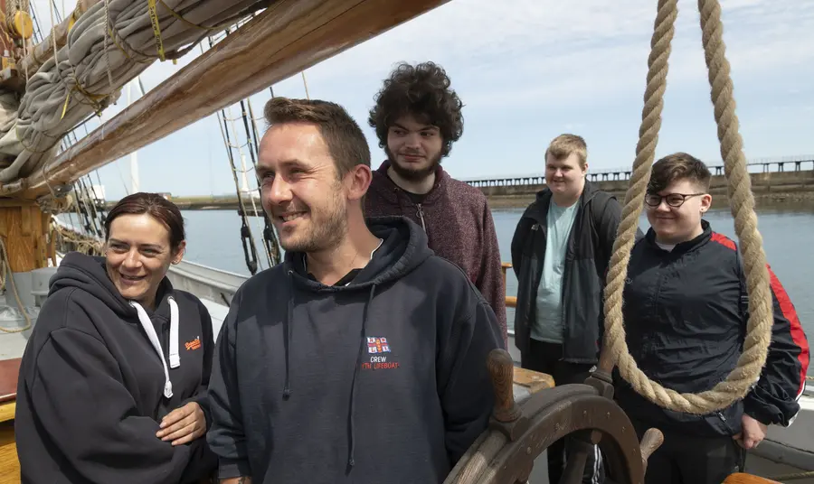 A group of young people standing on deck of a tall ship in dock.