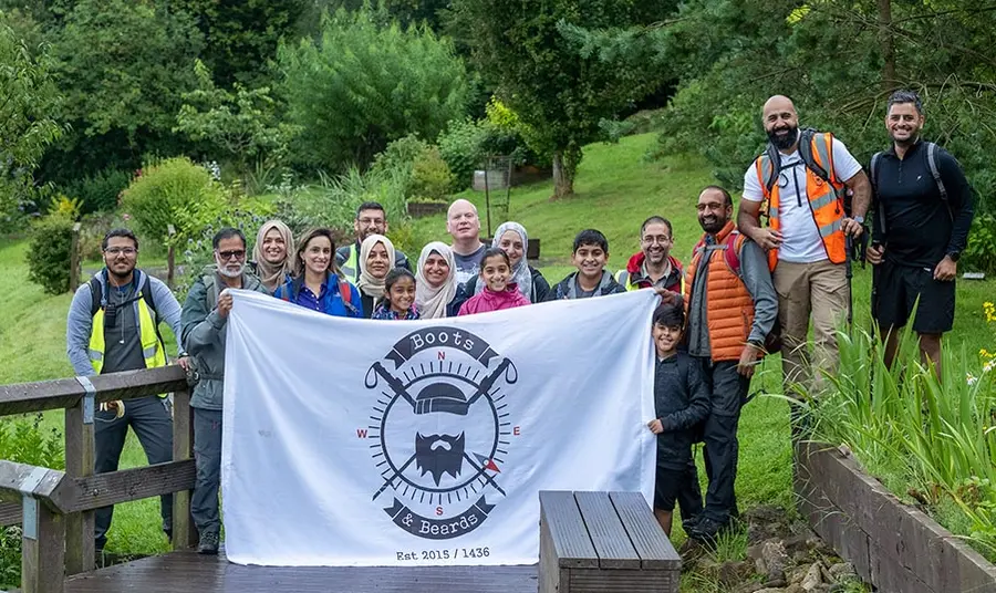 A group of South Asian people pose outdoors holding a flag with the logo of Boots and Beards