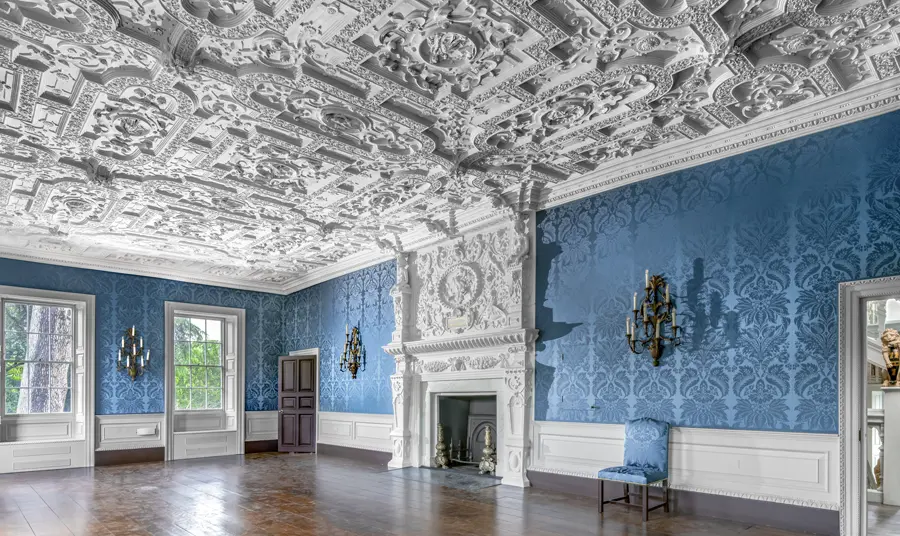 A room in the building with white intricate plaster ceiling and blue wallpaper