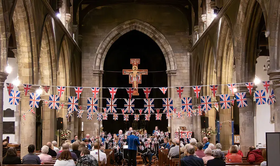 A brass band concert takes place in All Saints Hessle A brass band concert takes place inside All Saints Hessle. People can be seen sitting in the pews and the church is decorated with Union flags